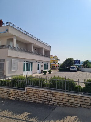 Un hotel de varios pisos con balcones, un estacionamiento y un muro de piedra al frente.