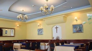 A dining area with tables and chairs, a chandelier, wall-mounted lights, and framed artwork. - Adria (Kastela)