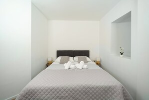 A hotel room with a bed, pillows, a nightstand, a lamp, and a small potted plant.