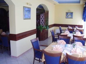 Un comedor con mesas dispuestas para el servicio, sillas y una planta decorativa.
