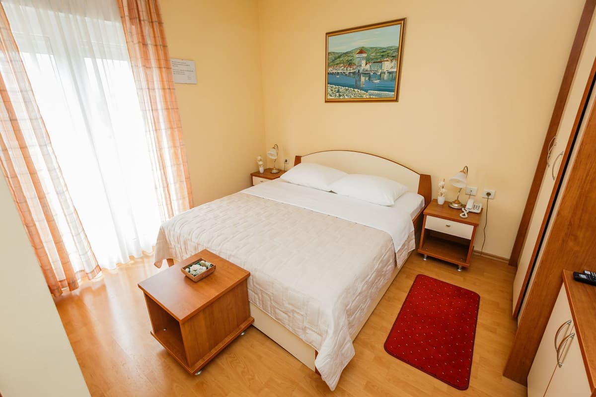 Quarto com cama, mesas de cabeceira, tapete vermelho e um quadro na parede.