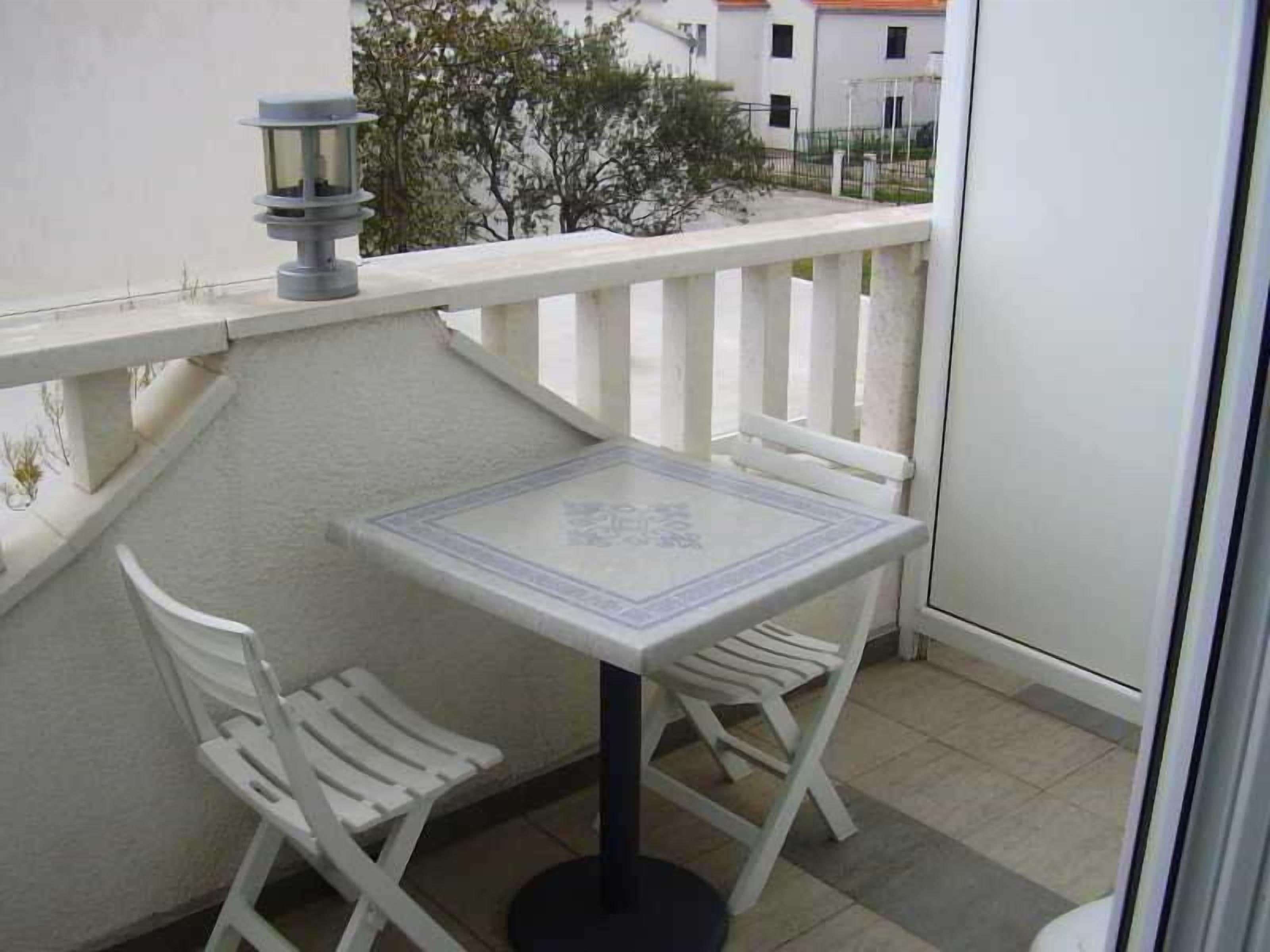Un balcón con una mesa y dos sillas, una planta en maceta y vistas de edificios al fondo.