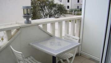 Un balcón con una mesa y dos sillas, una planta en maceta y vistas de edificios al fondo.