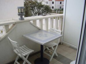 Un balcon avec une table et deux chaises, un pot de fleurs et une vue sur des bâtiments en arrière-plan.