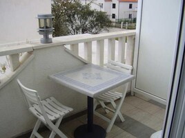 Un balcón con una mesa y dos sillas, una planta en maceta y vistas de edificios al fondo.