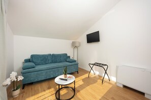 A living room with a teal sofa, a small round table with a remote, a floor lamp, and a radiator. - Adria (Kastela)