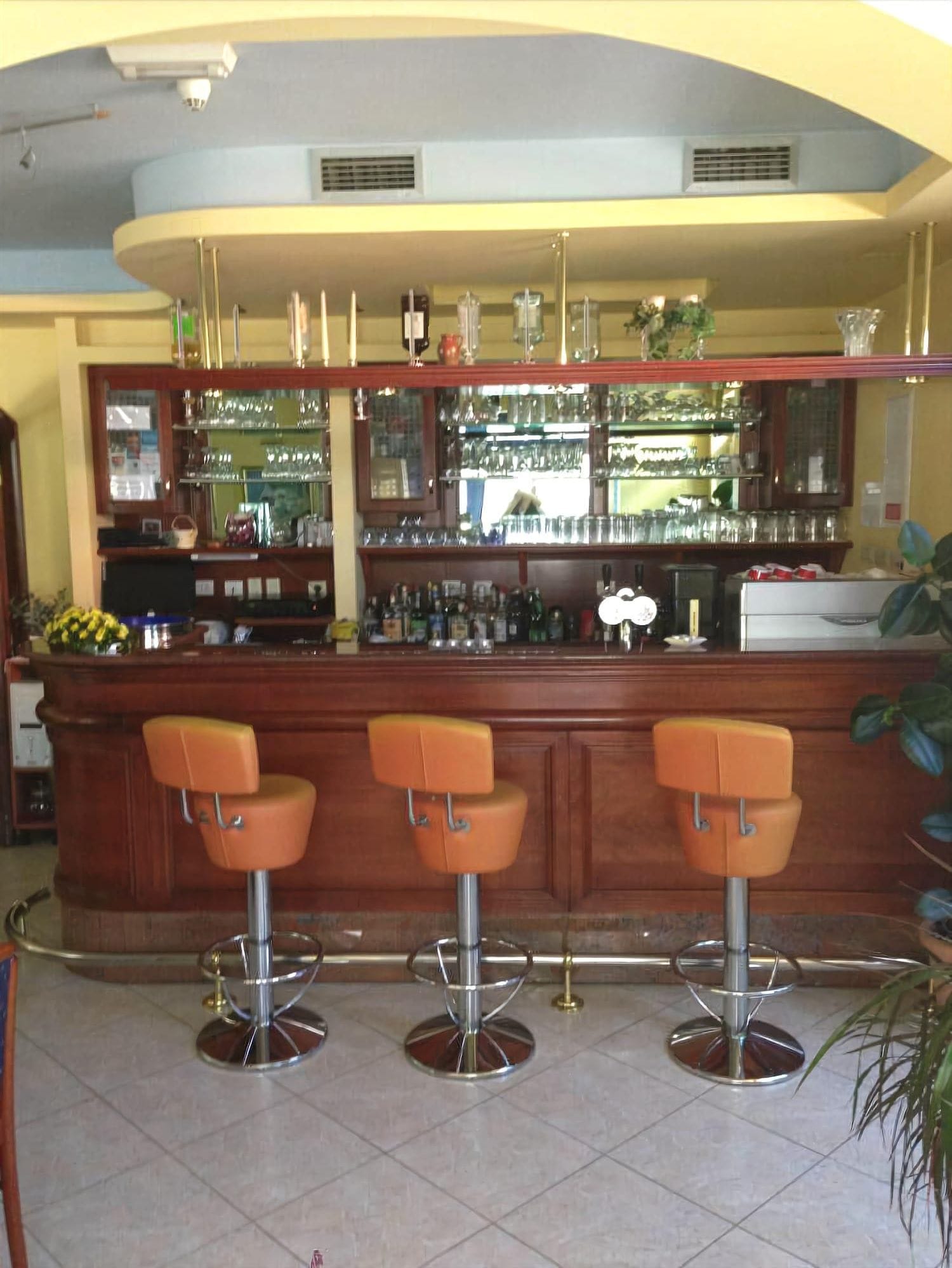 A bar area with a wooden counter, three bar stools, and shelves stocked with bottles and glasses.