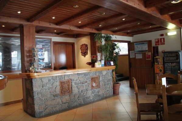 Una zona de recepción con mostrador de piedra, vigas de madera en el techo y una planta en maceta.