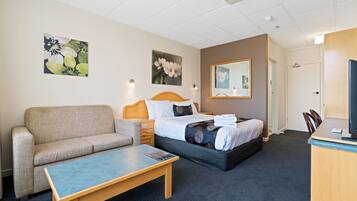 A hotel room with a bed, a sofa, a desk, and artwork on the walls.