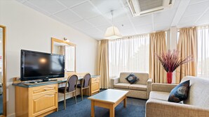 Une chambre d’hôtel équipée d’une télévision, d’un bureau en bois, de chaises, d’un canapé et d’une table basse.