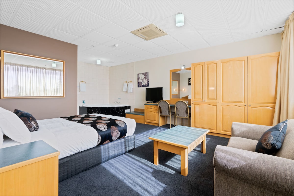 A hotel room with a bed, a desk, a chair, a sofa, and a wardrobe.