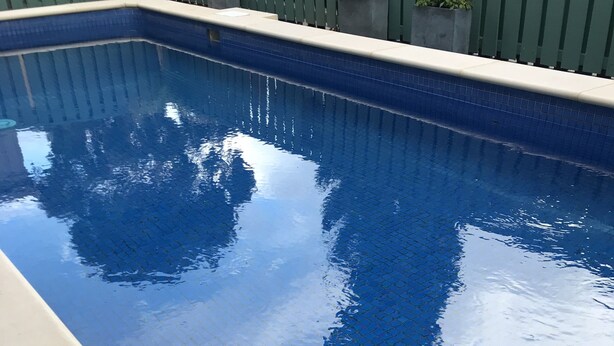 Une piscine rectangulaire, bordée de carreaux et entourée d’une terrasse de couleur claire.