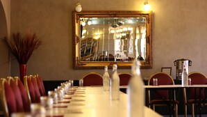 Un coin repas avec une longue table, des chaises à revêtement rouge et un grand miroir décoratif accroché au mur.