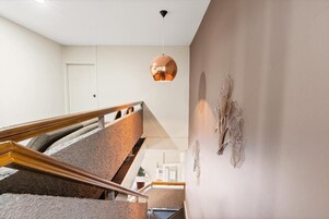 Una escalera con barandilla de madera y una lámpara colgante moderna.