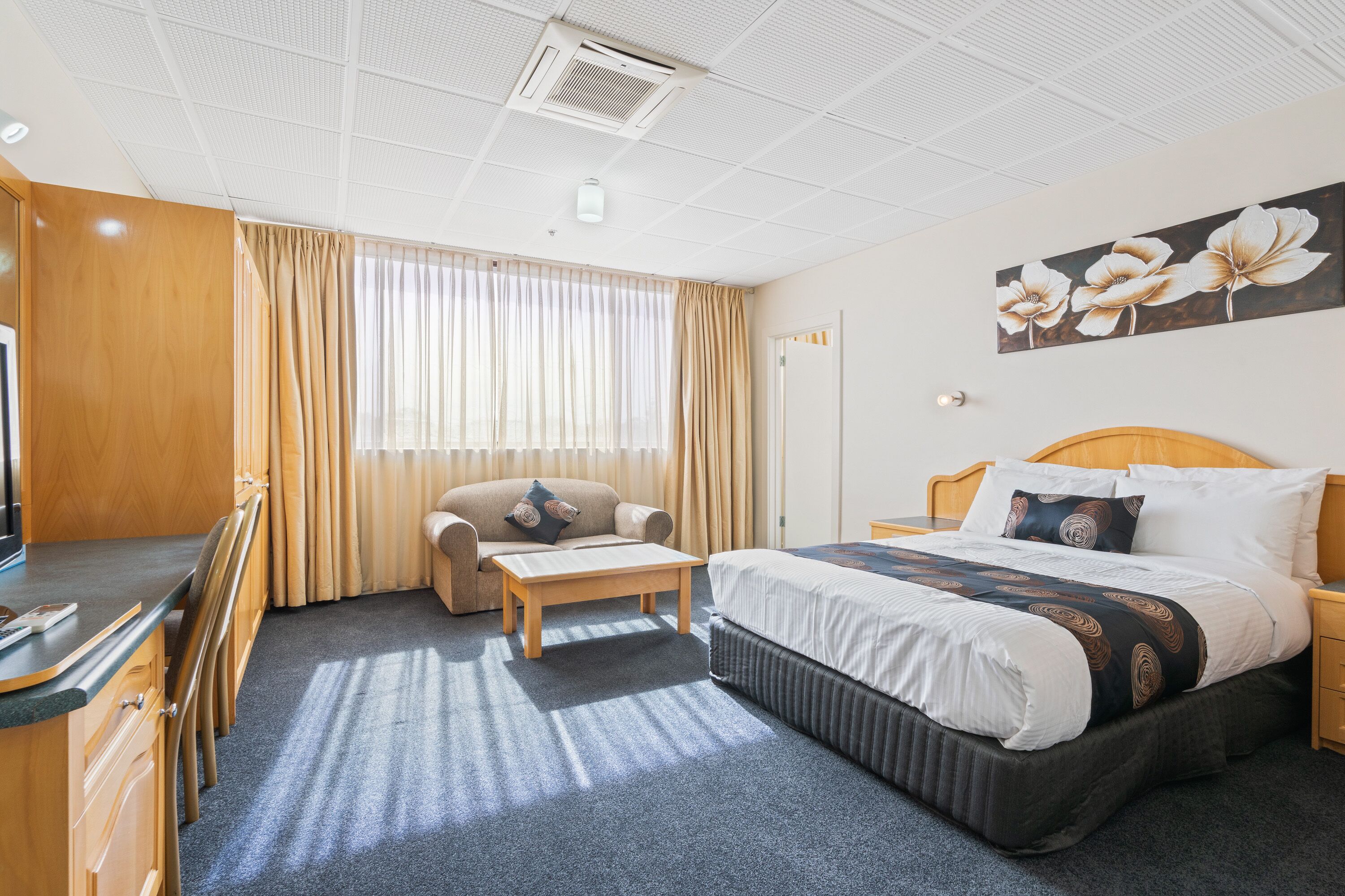 Une chambre d’hôtel avec un lit, un bureau, une chaise, une petite table et une fenêtre avec des rideaux.