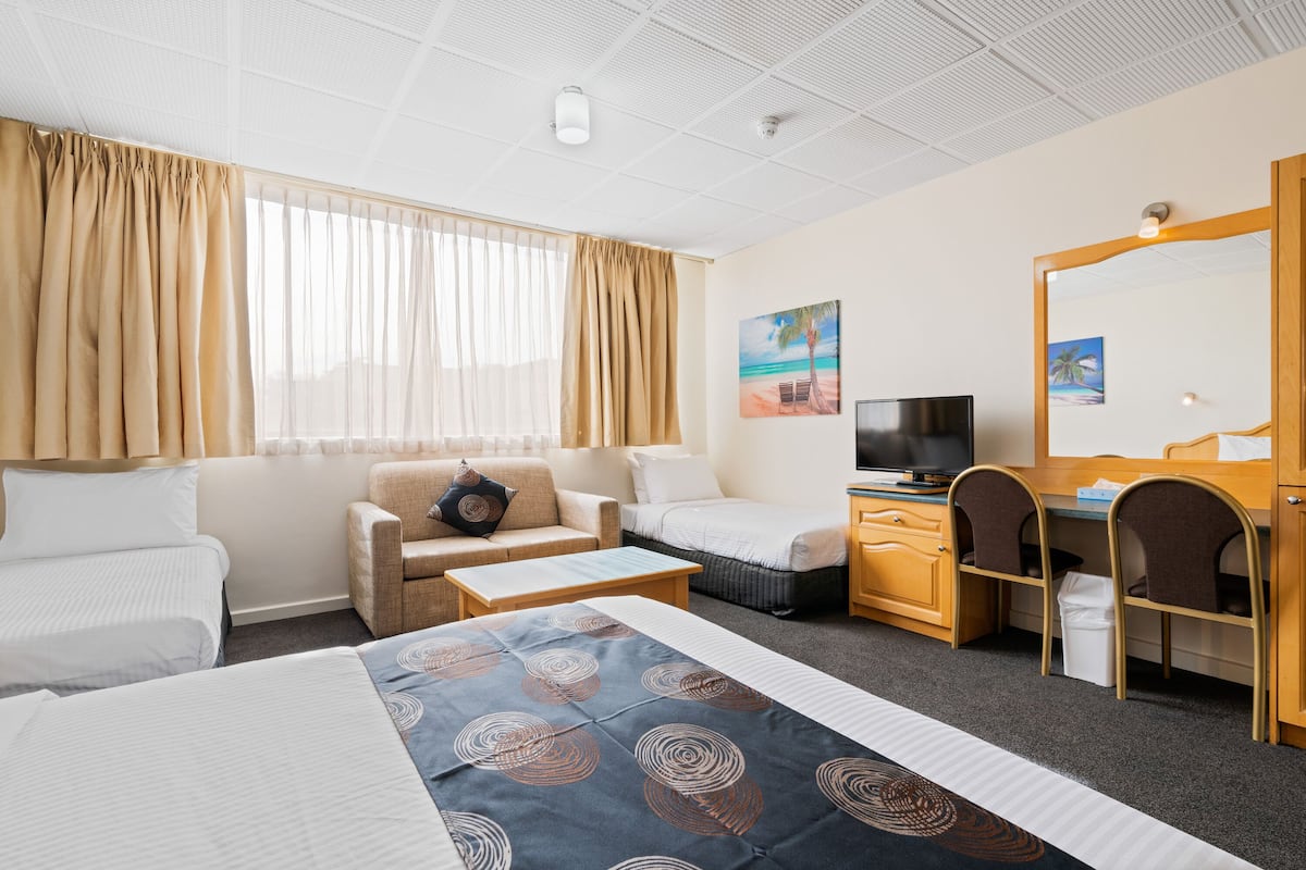 A hotel room with a bed, two sofas, a desk, a TV, and a large mirror.