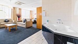 Une chambre d’hôtel moderne dotée d’un espace salon, d’une grande baignoire et offrant une vue sur la ville.