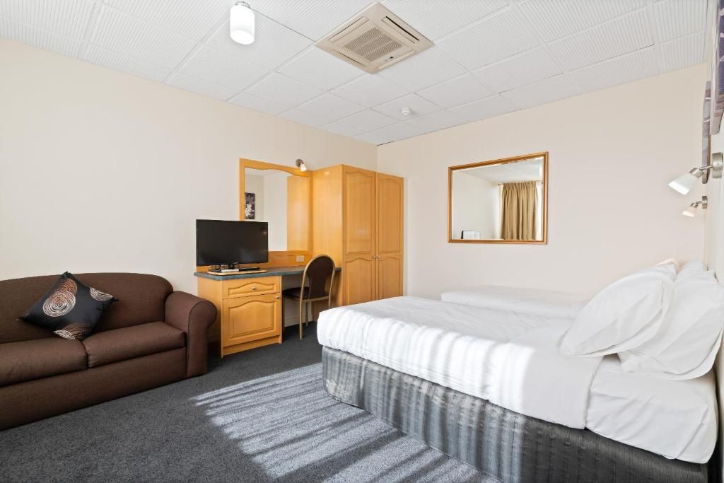 A hotel room with a bed, a desk with a television, a sofa, and a wardrobe.