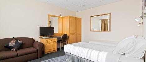 A hotel room with a bed, a desk with a television, a sofa, and a wardrobe.
