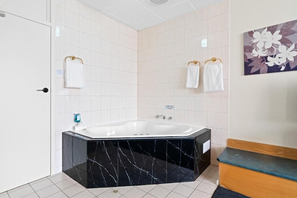 Un baño moderno con una bañera de mármol negro, paredes de azulejos blancos y un banco de madera.