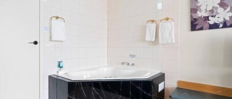 Un baño moderno con una bañera de mármol negro, paredes de azulejos blancos y un banco de madera.