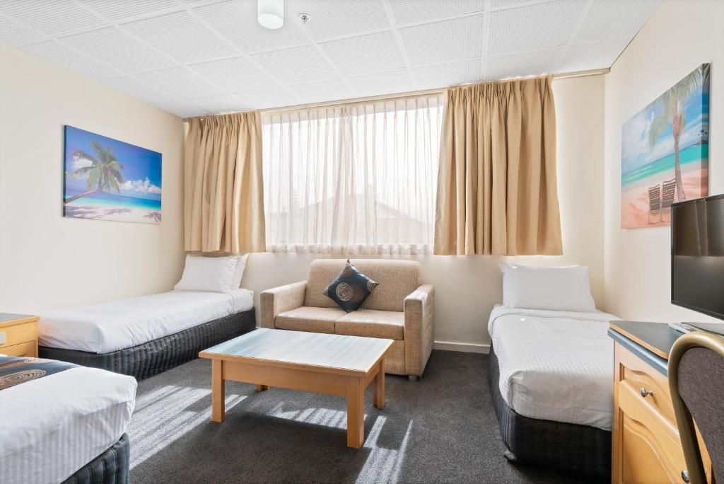 Habitación de hotel con dos camas individuales, un sofá, una mesa de centro y un televisor.