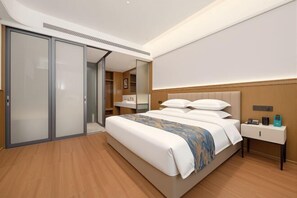 A modern hotel room with a large bed, a bedside table with a lamp, a wardrobe, and a mirror.