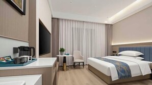 Ein Hotelzimmer mit einem Bett, einem Schreibtisch mit Kaffeemaschine, einem Sessel und einem Fernseher.
