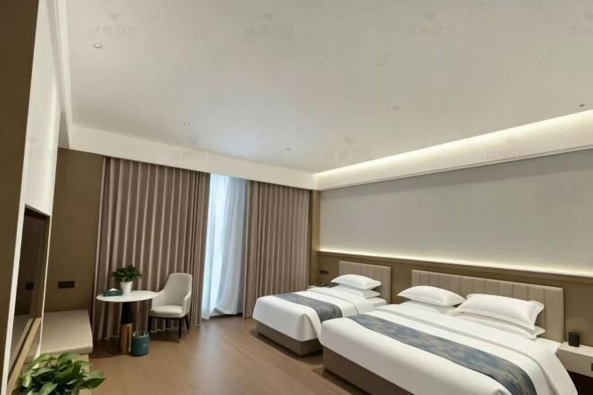 A hotel room with two beds, a desk, a chair, and a large window with curtains.