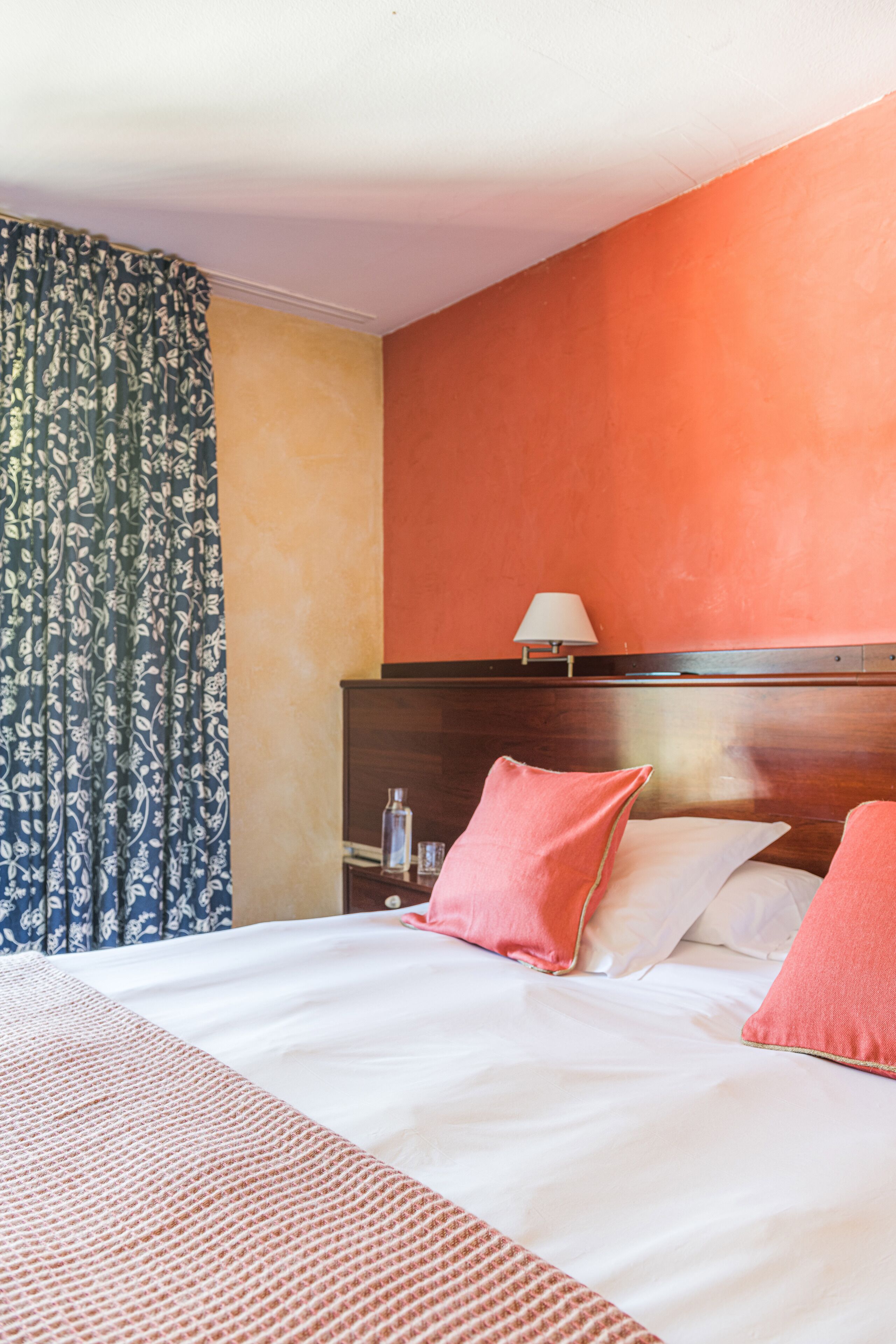 A hotel room with a bed, a nightstand, a lamp, and a window with curtains.