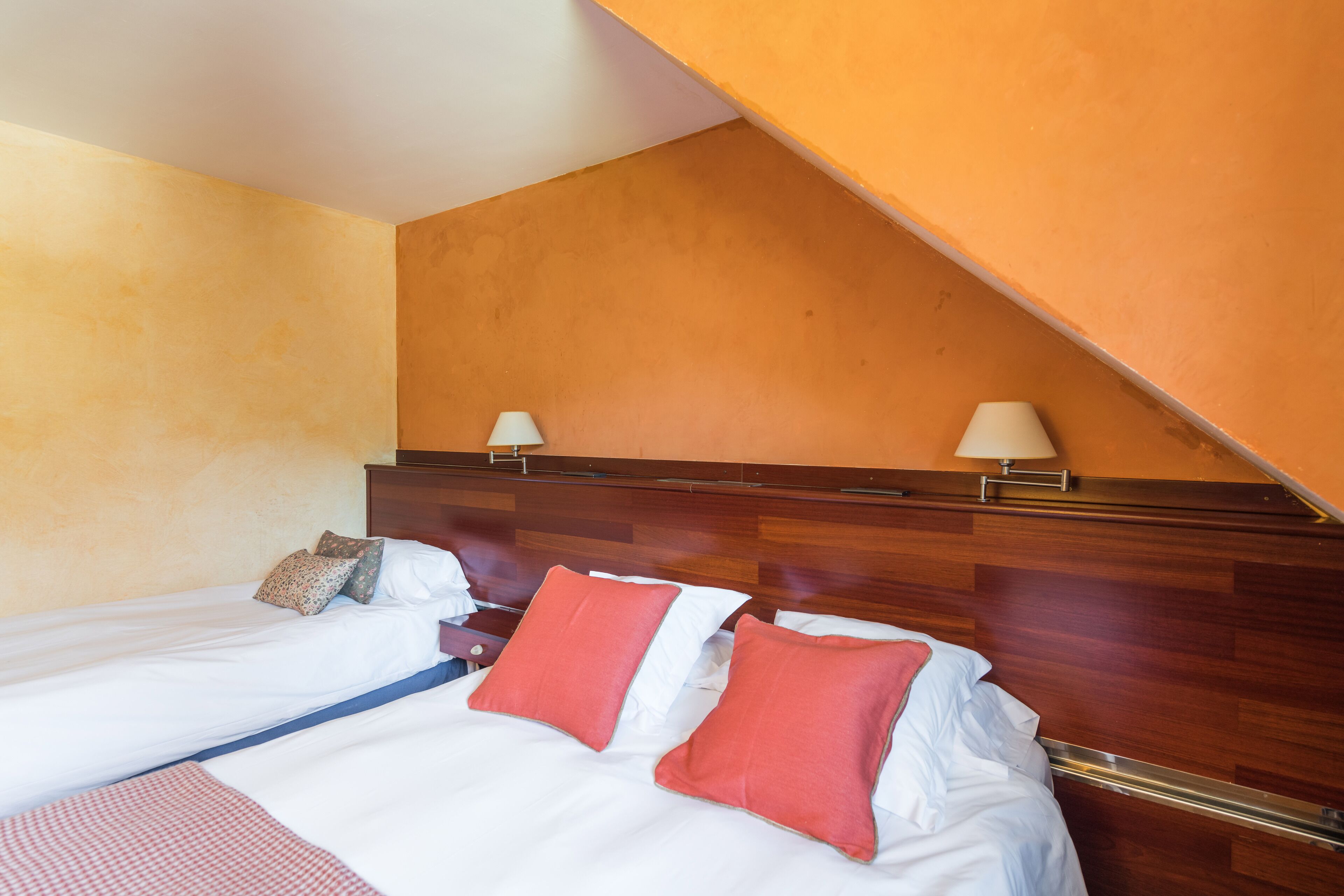 Una habitación de hotel con dos camas individuales, cabeceros de madera y techo inclinado.