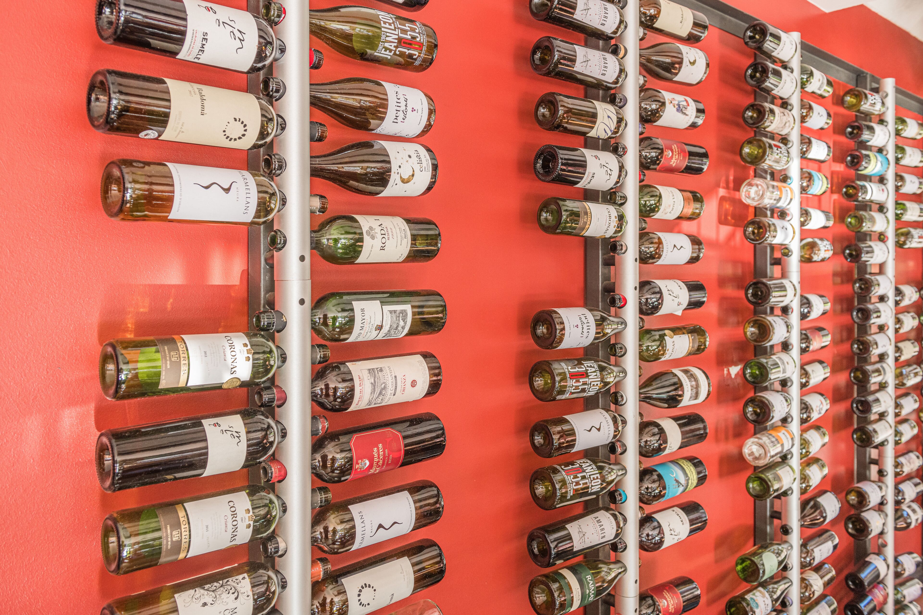 A wall of wine bottles arranged in rows on a red background.