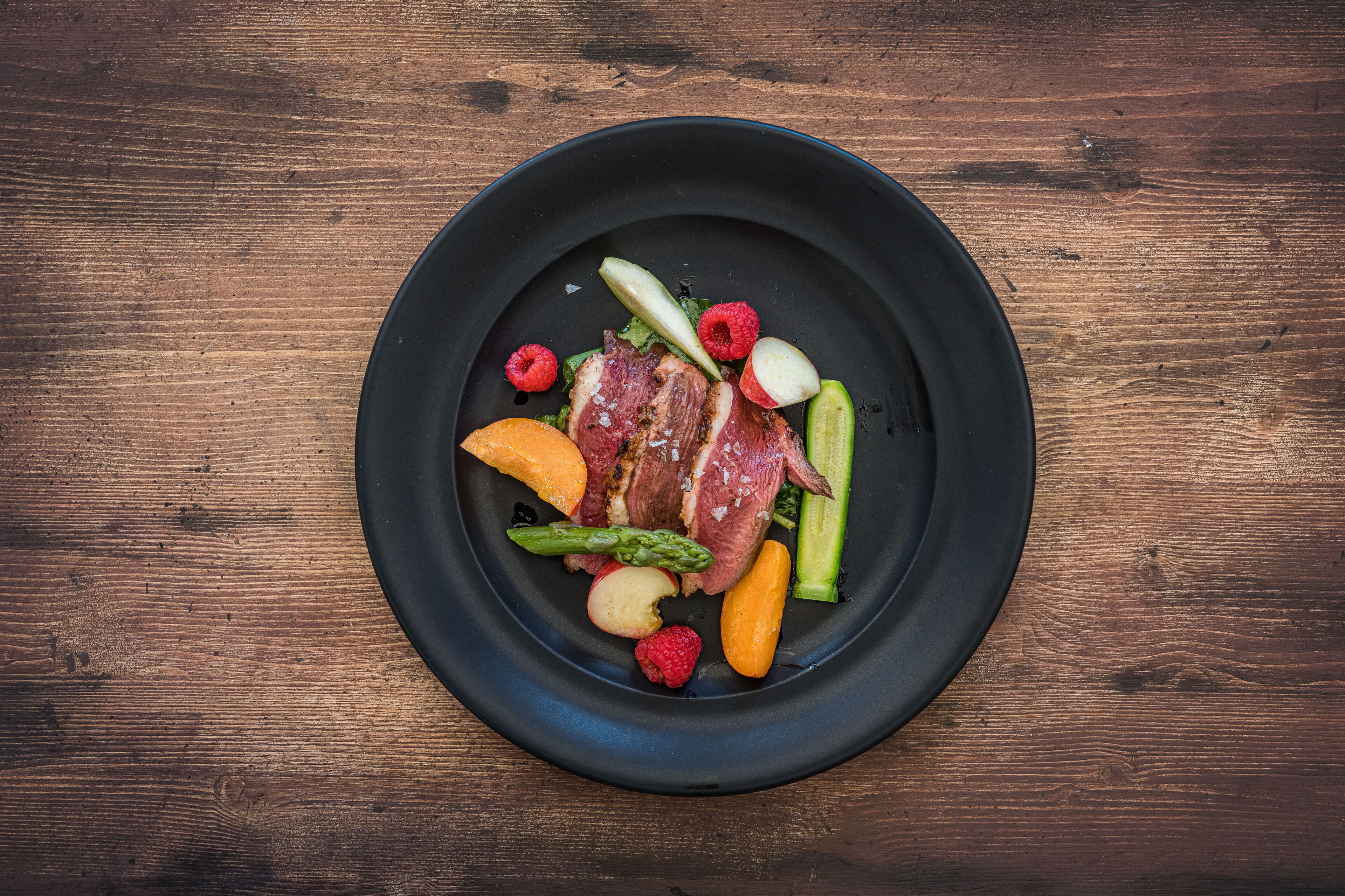 A black plate with a variety of fruits and vegetables on a wooden table.