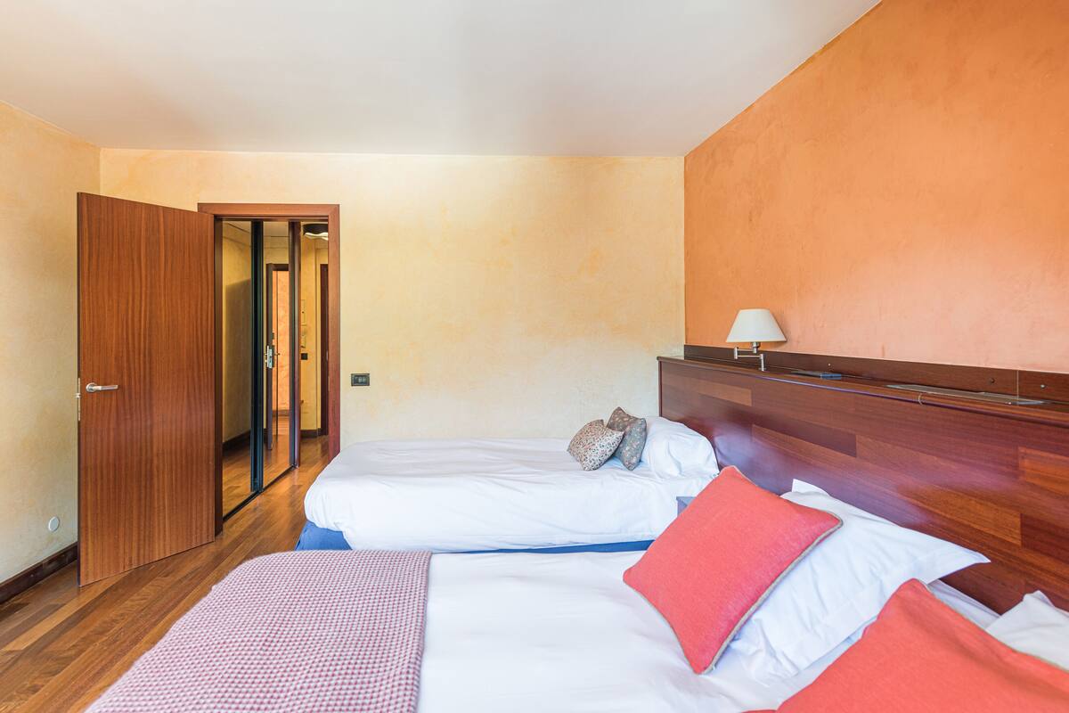 A hotel room with two beds, wooden flooring, a wooden headboard, and a door leading to another room.