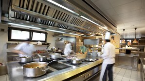 Una cocina comercial con electrodomésticos de acero inoxidable, una estufa grande y chefs trabajando.