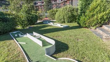 Un campo de mini golf con césped artificial verde, rodeado de árboles y un telón de fondo montañoso.