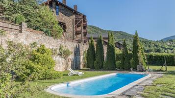 Ein Gebäude aus Stein mit einem Pool, umgeben von Grünflächen und Hügeln.