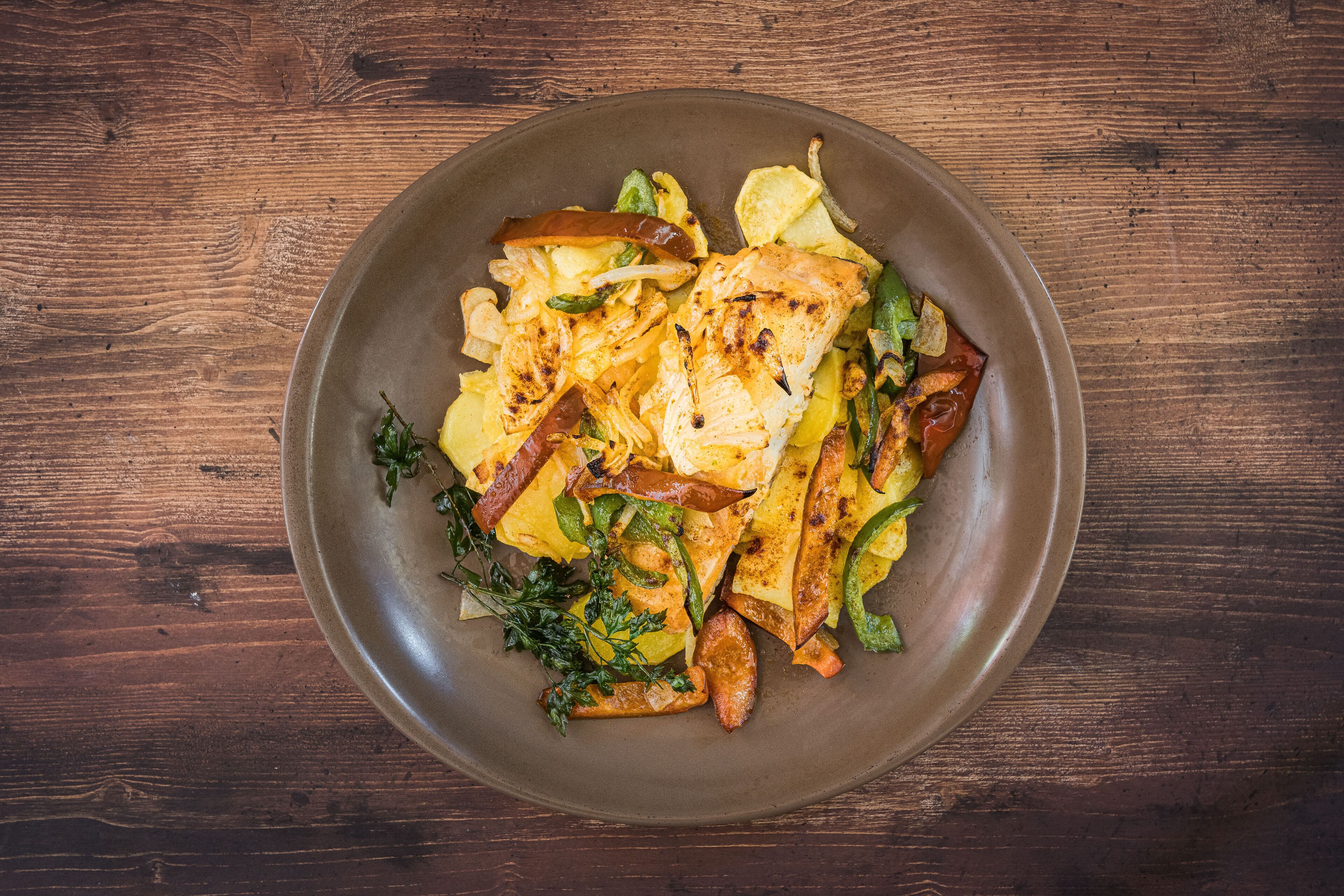 Une assiette de nourriture contenant des légumes et des pommes de terre grillés, posée sur une table en bois.