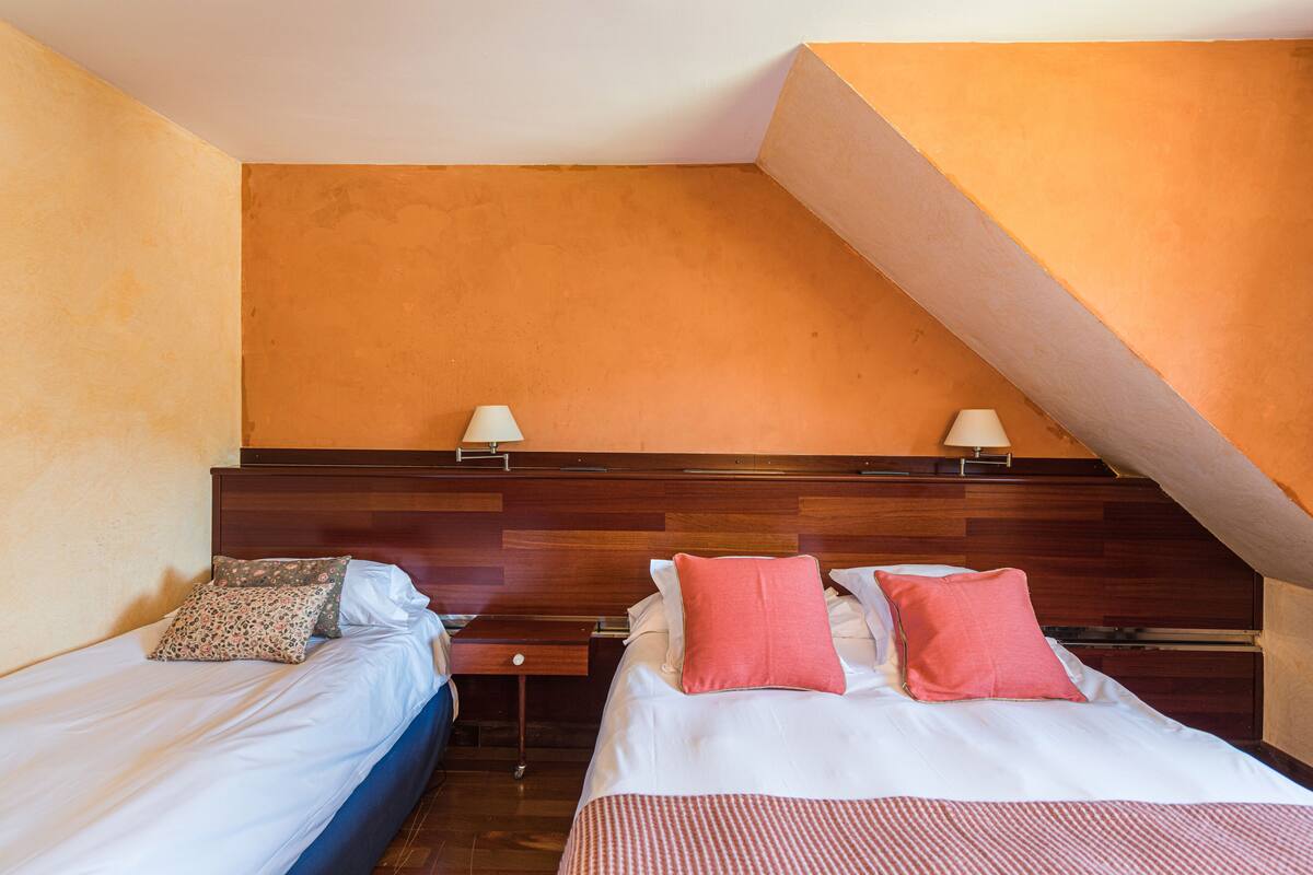 A hotel room with two beds, wooden headboards, and a sloped ceiling.
