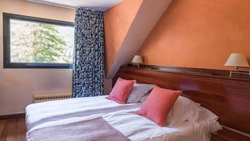 Habitación de hotel con una cama grande, dos mesitas de noche, una ventana con cortinas y vistas a árboles.