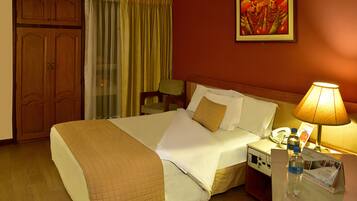 A hotel room with a bed, a nightstand with a lamp, a telephone, and a brochure on the nightstand.
