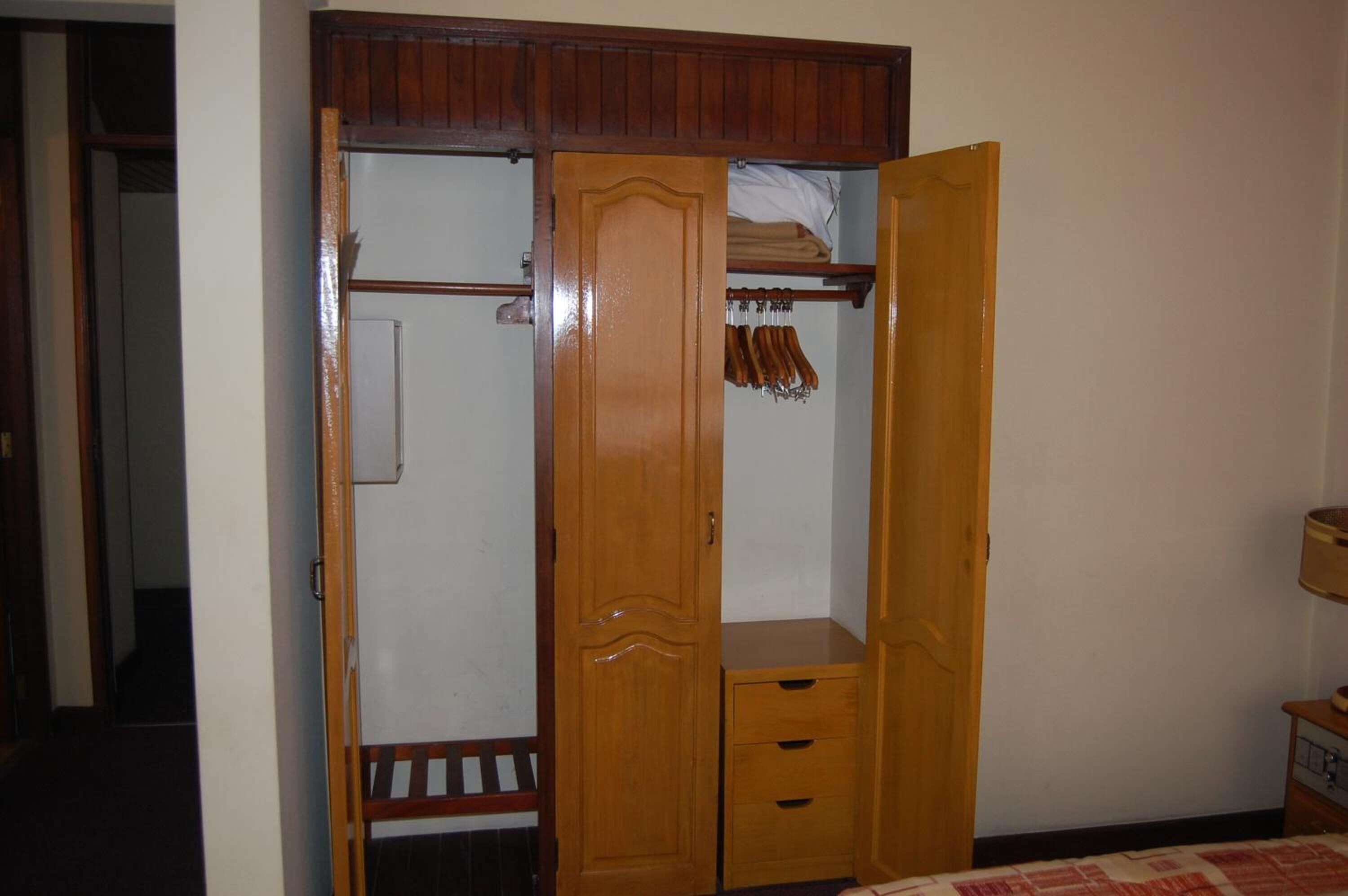 A wooden wardrobe with a mirror, a hanging rod, and a shelf.