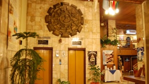 A lobby with a stone wall, two elevators, potted plants, a reception desk, and a religious statue. - Cesars Plaza Hotel (Cochabamba)