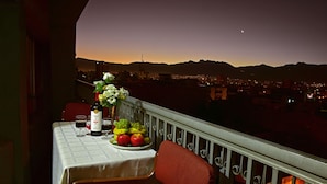 A balcony with a table set for dining, a vase with flowers, and a view of a cityscape at dusk. - Cesars Plaza Hotel (Cochabamba)