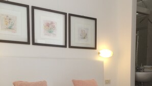 A neatly made bed with white and pink pillows, a folded towel with a pink rose, and three framed artworks on the wall above. - Hotel Pinocchio (Cattolica)