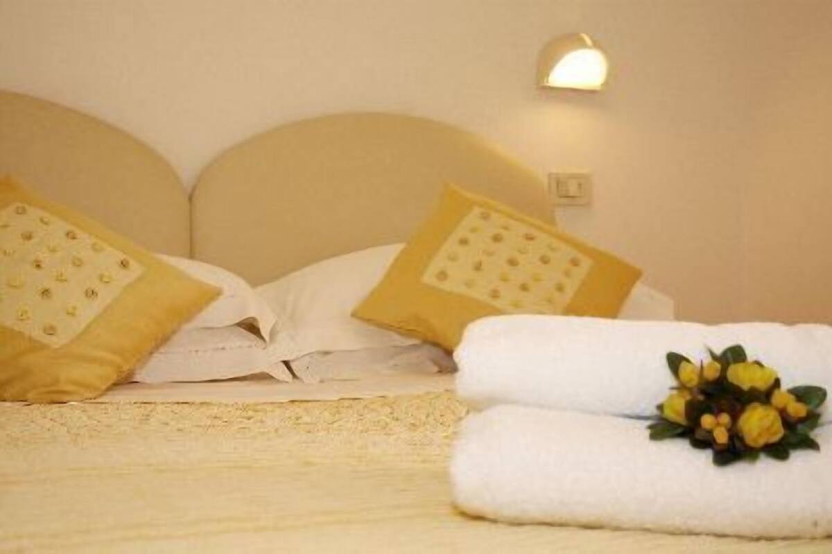 A neatly made bed with white linens and two pillows, one with a yellow pattern and the other plain.