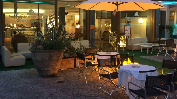 A hotel patio with outdoor seating, a large umbrella, and a visible restaurant area. - Hotel Pinocchio (Cattolica)