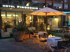 Un patio de hotel con mesas al aire libre, un paraguas grande y una zona de restaurante visible.