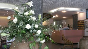 A reception area with a large floral arrangement, a reception desk, and a wicker chair. - Hotel Pinocchio (Cattolica)