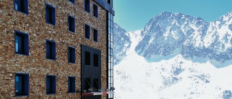 Un hotel de ladrillo con numerosas ventanas, con vistas a una cadena montañosa cubierta de nieve.